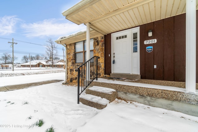 snow covered property entrance featuring stone siding