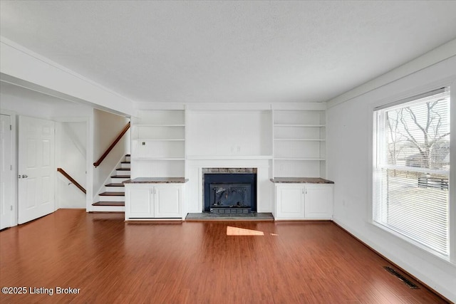 unfurnished living room with built in features, a high end fireplace, hardwood / wood-style floors, and a textured ceiling