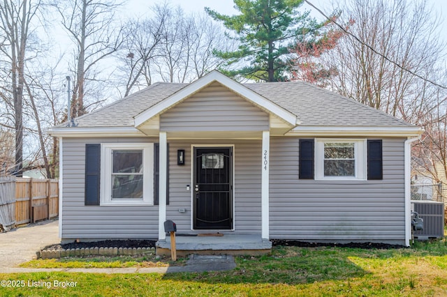 bungalow-style house with a porch, central air condition unit, fence, and a shingled roof