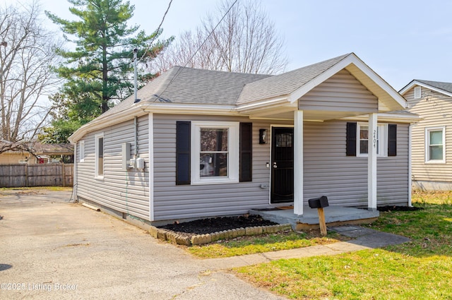 bungalow-style home featuring driveway, roof with shingles, and fence