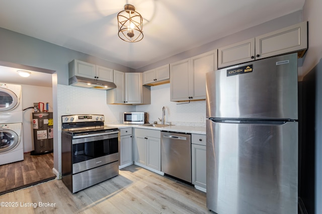 kitchen with stacked washer and dryer, a sink, electric water heater, appliances with stainless steel finishes, and light countertops