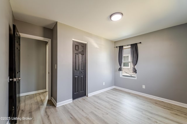 unfurnished bedroom featuring light wood-type flooring, baseboards, and a closet