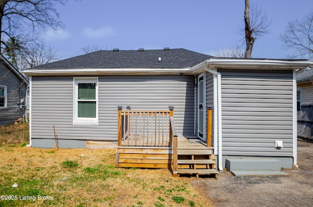 rear view of property featuring fence, roof with shingles, and a wooden deck