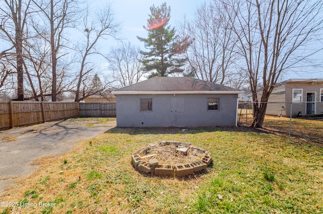 back of property featuring concrete block siding, a fenced backyard, a lawn, and an outdoor fire pit