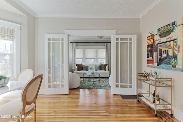 living area with wood-type flooring, a textured ceiling, crown molding, and french doors