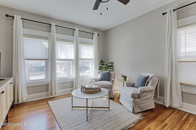 living area with ceiling fan, light hardwood / wood-style flooring, and a textured ceiling