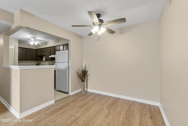 kitchen featuring ceiling fan, white fridge, dark brown cabinetry, kitchen peninsula, and light wood-type flooring