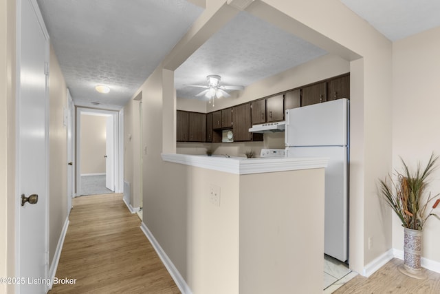 kitchen featuring dark brown cabinetry, a textured ceiling, light wood-type flooring, white refrigerator, and kitchen peninsula