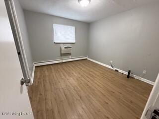 empty room with an AC wall unit, hardwood / wood-style floors, and a baseboard heating unit