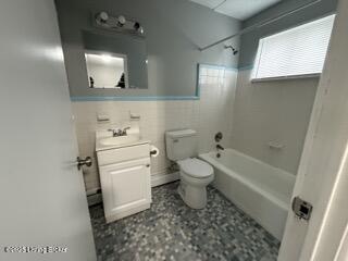 full bathroom featuring vanity, tiled shower / bath combo, tile walls, and toilet