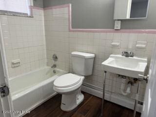 bathroom with tile walls, hardwood / wood-style floors, tiled shower / bath combo, a baseboard heating unit, and toilet