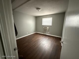 empty room with a wall mounted air conditioner and dark wood-type flooring