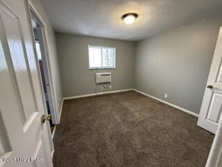 unfurnished room featuring an AC wall unit and dark colored carpet