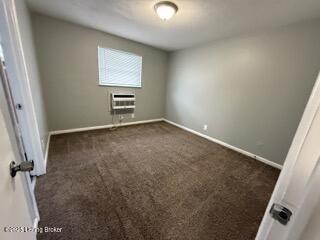 spare room featuring a wall mounted AC and dark colored carpet