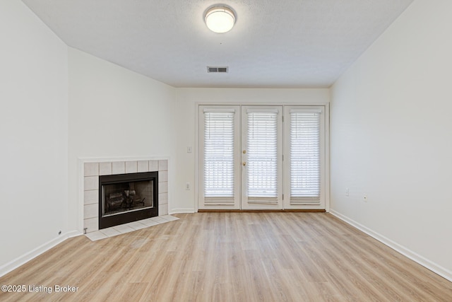 unfurnished living room with a textured ceiling, a tile fireplace, wood finished floors, visible vents, and baseboards