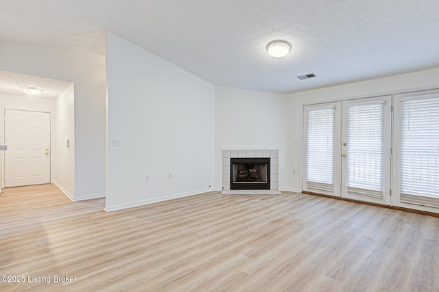 unfurnished living room with light wood-type flooring, baseboards, visible vents, and a tiled fireplace