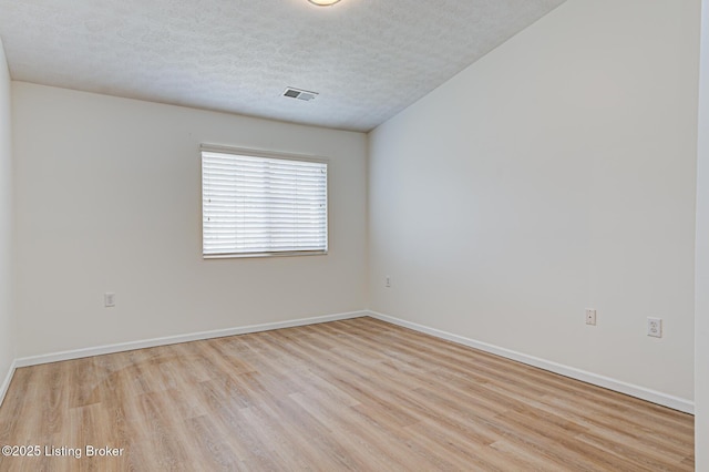 empty room with light wood-style floors, visible vents, a textured ceiling, and baseboards