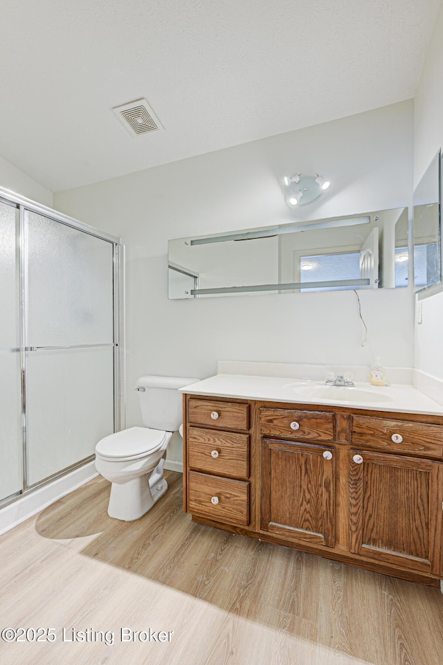 bathroom featuring toilet, a stall shower, visible vents, and wood finished floors