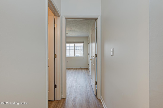 hall featuring a textured ceiling, baseboards, and wood finished floors