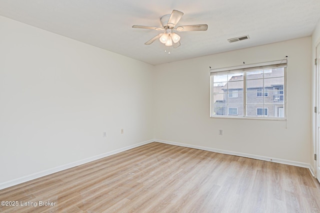 spare room featuring light wood finished floors, baseboards, visible vents, and a ceiling fan