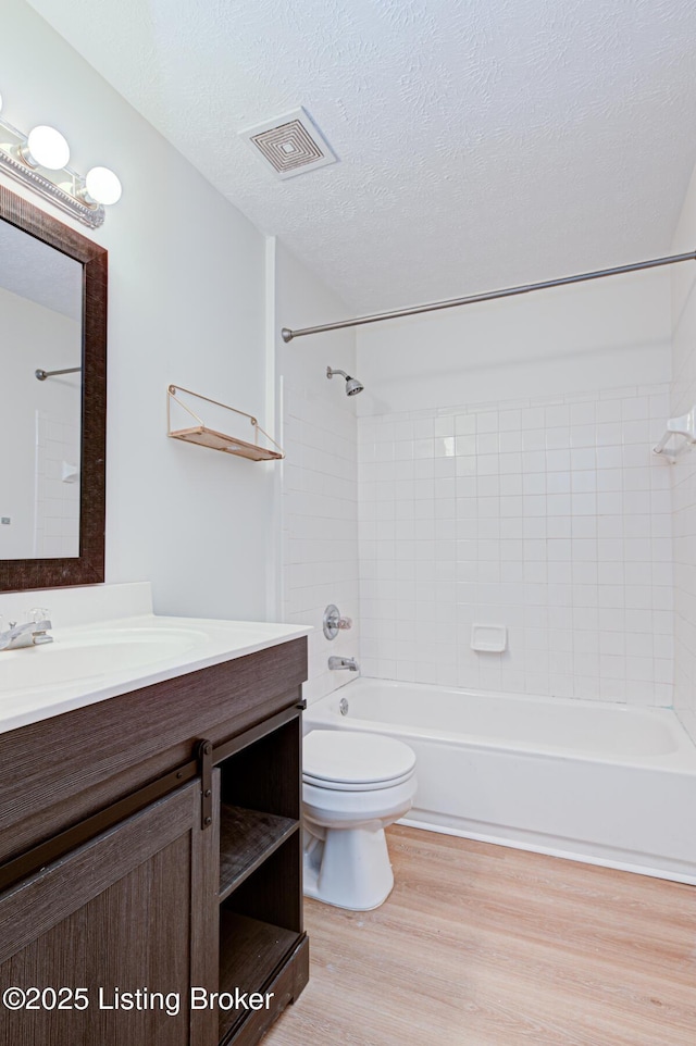 bathroom with visible vents, toilet, wood finished floors,  shower combination, and a textured ceiling