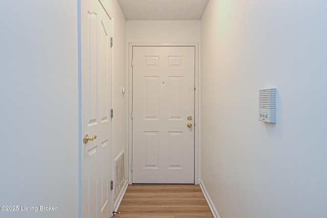 entryway with a textured ceiling, visible vents, light wood-style flooring, and baseboards