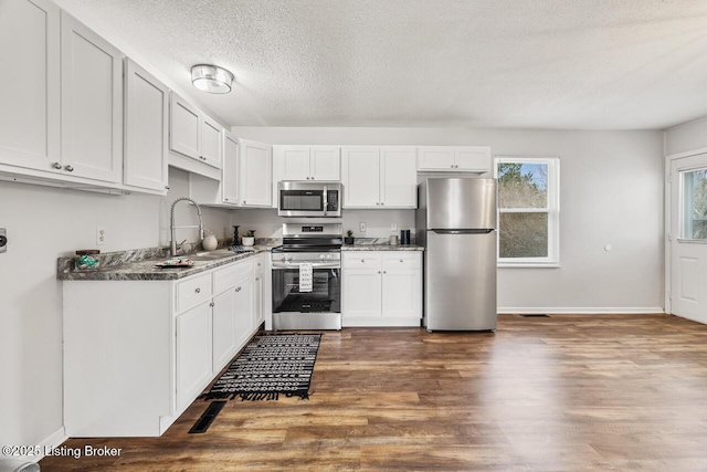 kitchen with sink, appliances with stainless steel finishes, dark hardwood / wood-style floors, a textured ceiling, and white cabinets