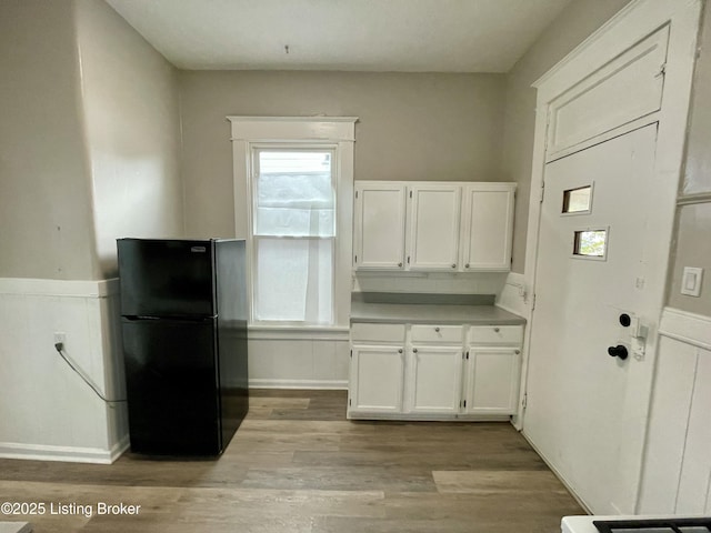 kitchen with black fridge, white cabinets, and light wood-type flooring