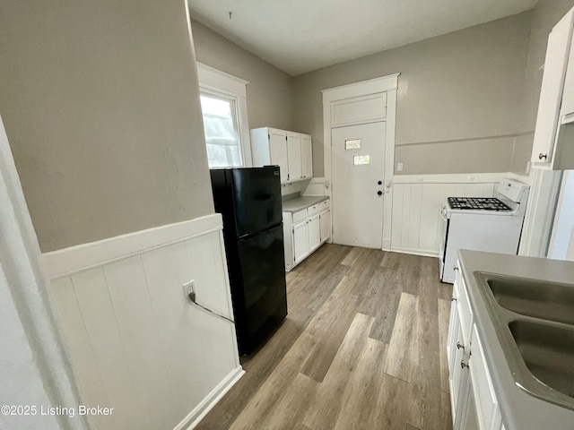 kitchen with sink, white range with gas stovetop, black fridge, white cabinetry, and light hardwood / wood-style floors