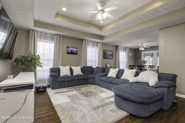 living room with a textured ceiling, ceiling fan, dark wood-style flooring, baseboards, and a tray ceiling