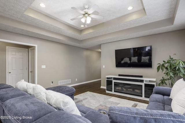 living area with dark wood-style floors, a tray ceiling, visible vents, a textured ceiling, and baseboards