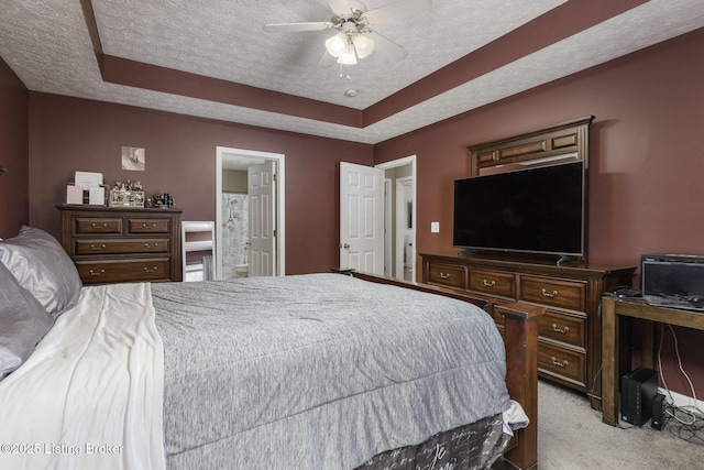 bedroom with a raised ceiling, connected bathroom, a ceiling fan, light colored carpet, and a textured ceiling