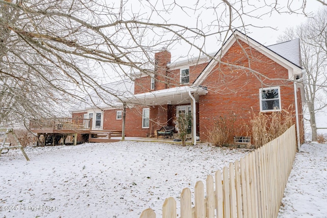 snow covered back of property with a wooden deck