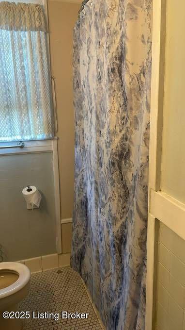 bathroom featuring a shower with shower curtain, toilet, and tile patterned floors