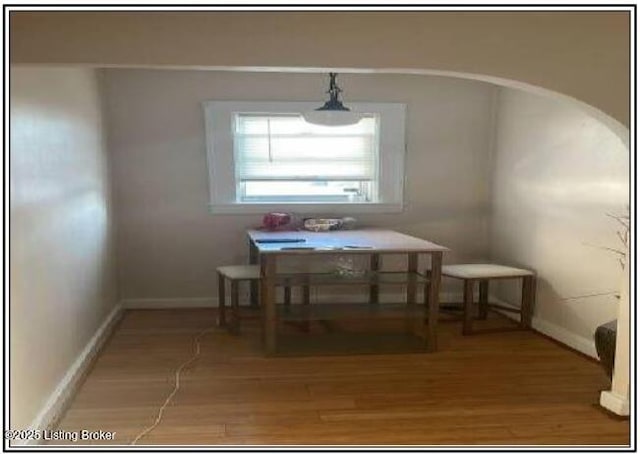 unfurnished dining area with light wood-style flooring, arched walkways, and baseboards