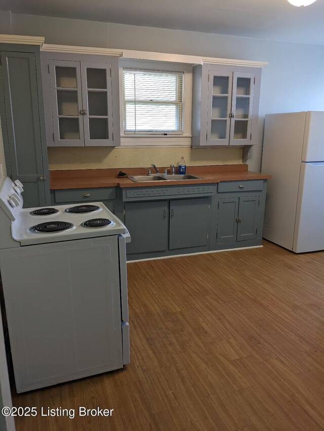 kitchen with wood finished floors, white appliances, a sink, and glass insert cabinets