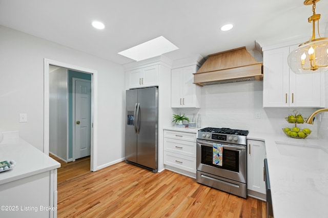 kitchen featuring sink, custom exhaust hood, white cabinetry, decorative light fixtures, and appliances with stainless steel finishes