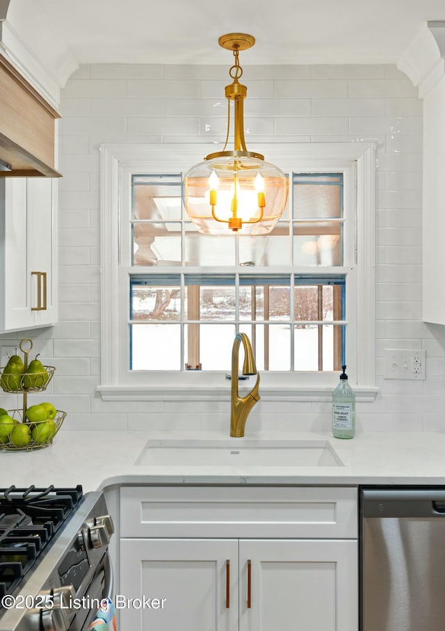 kitchen with pendant lighting, tasteful backsplash, sink, white cabinets, and stainless steel dishwasher