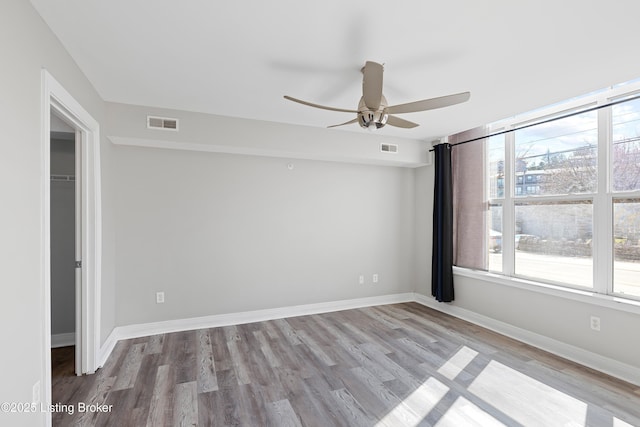 unfurnished room featuring a ceiling fan, wood finished floors, visible vents, and baseboards