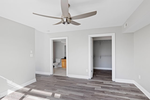 unfurnished bedroom with wood finished floors, visible vents, baseboards, a closet, and a walk in closet