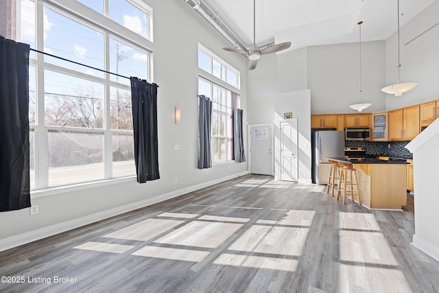 kitchen with light wood-style flooring, decorative backsplash, glass insert cabinets, appliances with stainless steel finishes, and dark countertops