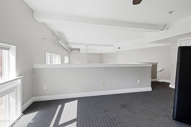 spare room featuring dark colored carpet, baseboards, and a healthy amount of sunlight