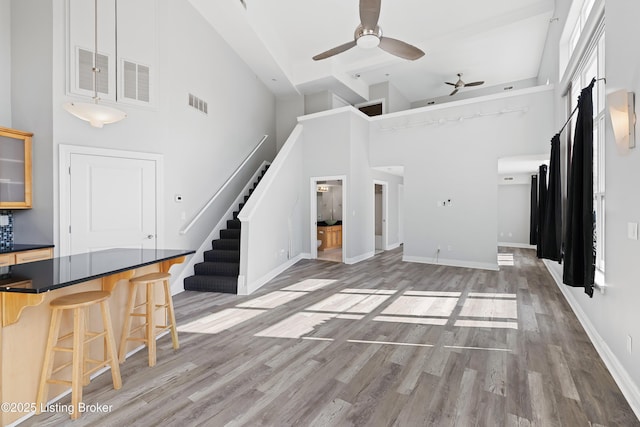 unfurnished living room with light wood-type flooring, visible vents, ceiling fan, and stairs