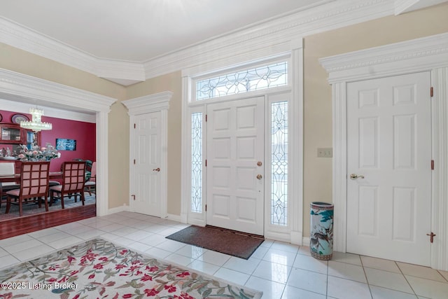 tiled entryway with ornamental molding and a notable chandelier