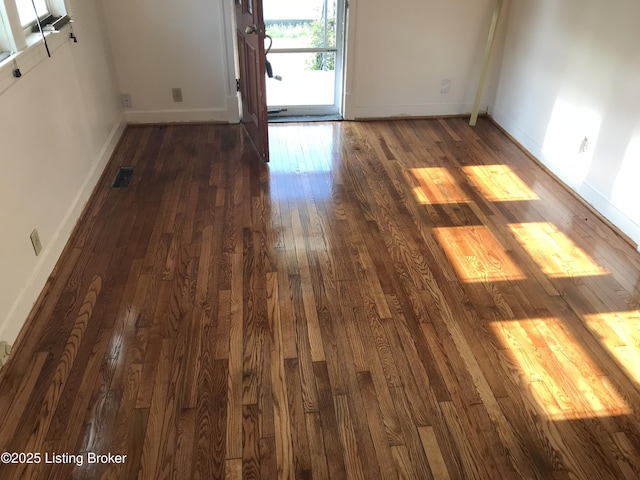 spare room with dark wood-style floors, visible vents, and baseboards