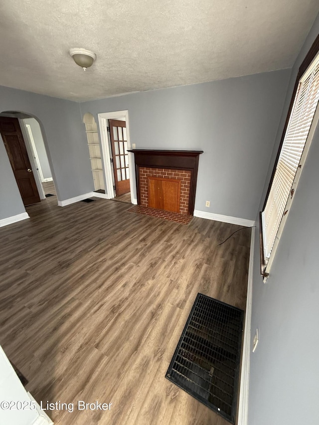 living room with arched walkways, a fireplace, wood finished floors, and baseboards