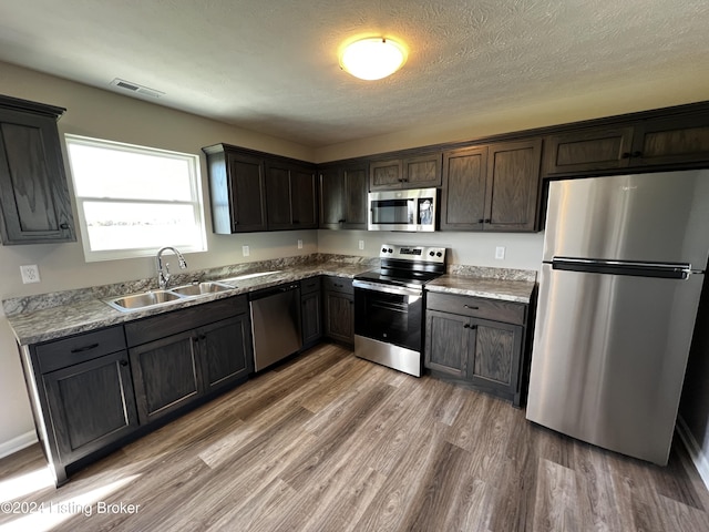 kitchen featuring sink, hardwood / wood-style flooring, stainless steel appliances, dark brown cabinetry, and a textured ceiling