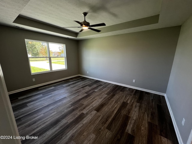 unfurnished room featuring ceiling fan, dark hardwood / wood-style flooring, a raised ceiling, and a textured ceiling