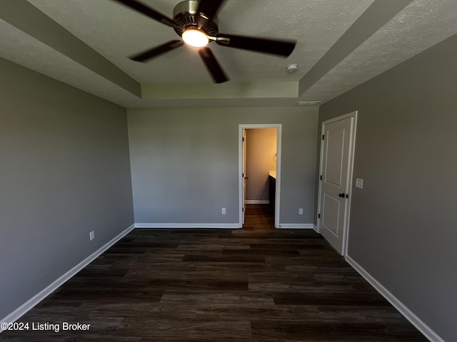 unfurnished bedroom featuring a tray ceiling, dark hardwood / wood-style flooring, a textured ceiling, and a spacious closet