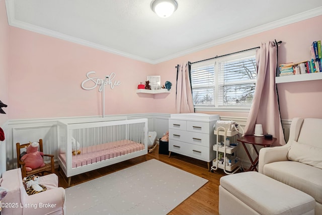 bedroom featuring a crib, crown molding, and hardwood / wood-style floors